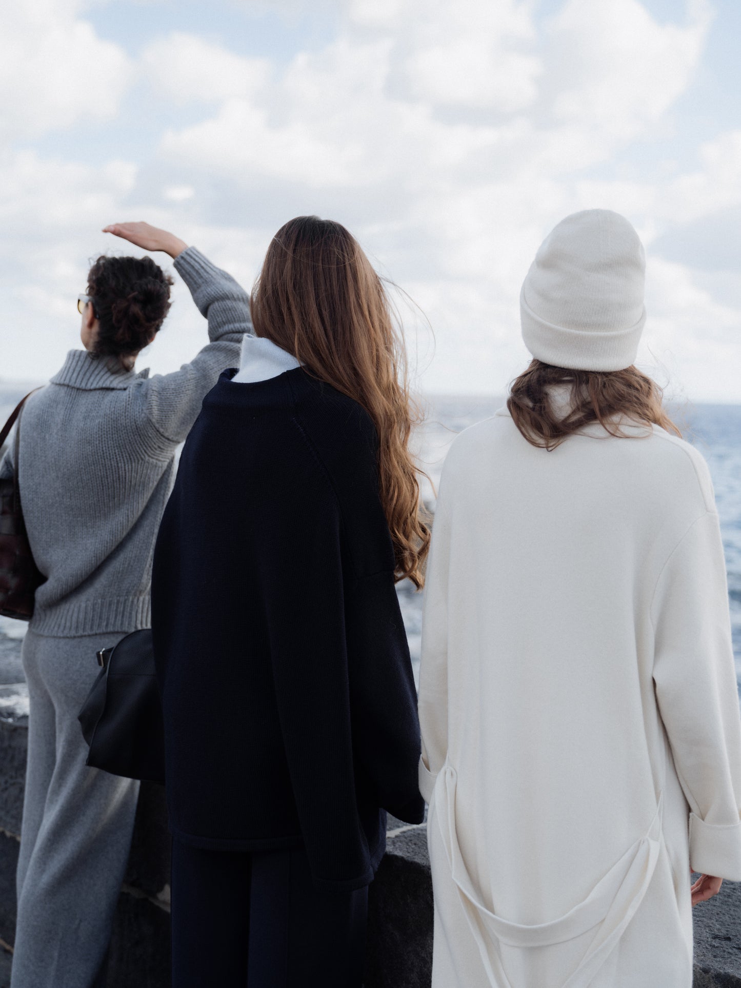 Three people standing on a beach, looking out towards the ocean.