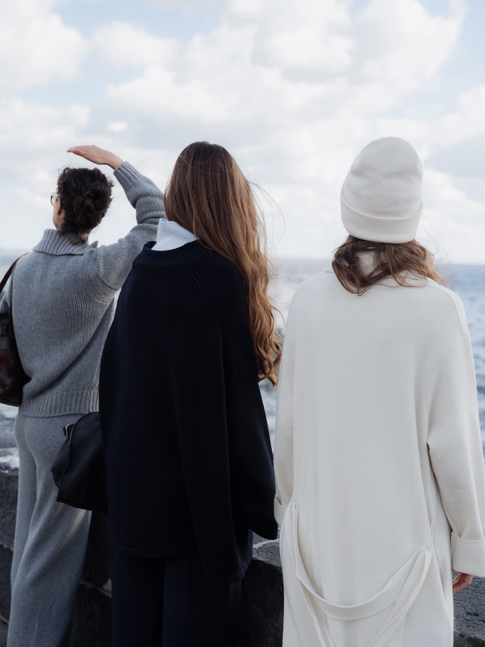 Three people standing on a beach, looking out towards the ocean.